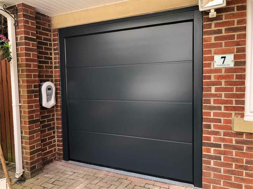 Black vertical ribbed garage door next to a wooden garden gate