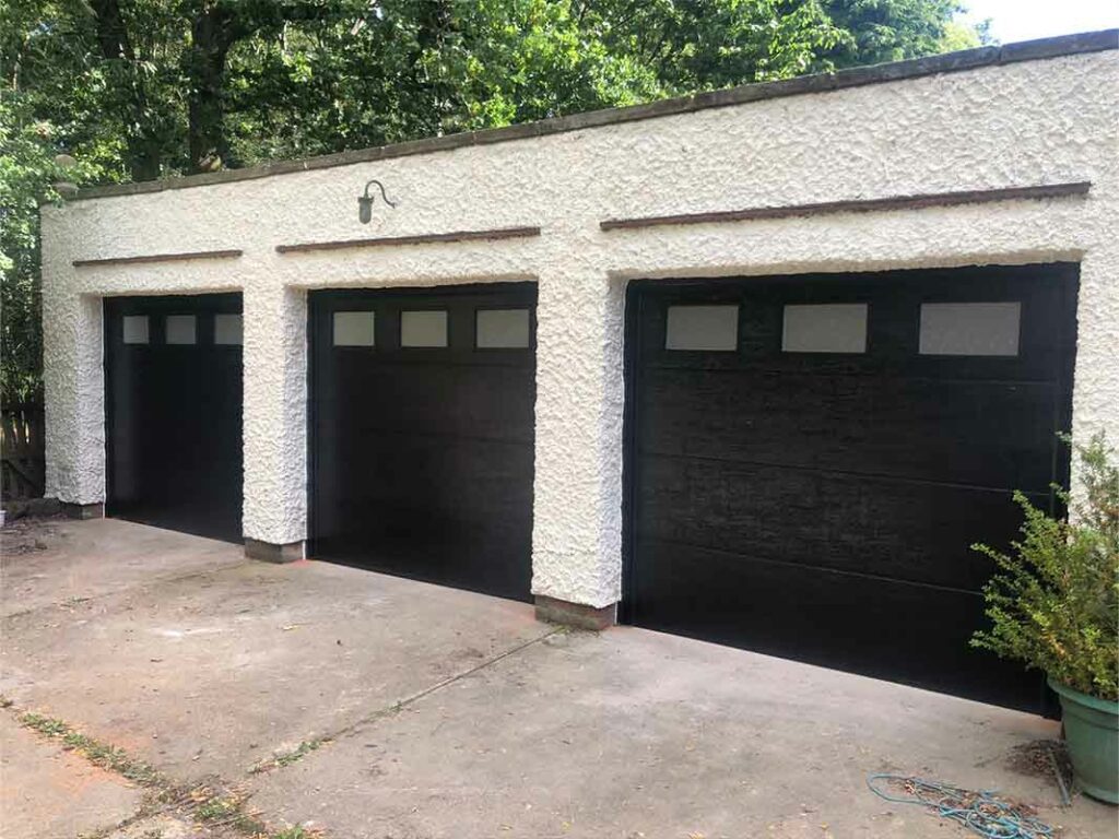 Two black traditional sectional garage doors with square windows on a white-rendered garage
