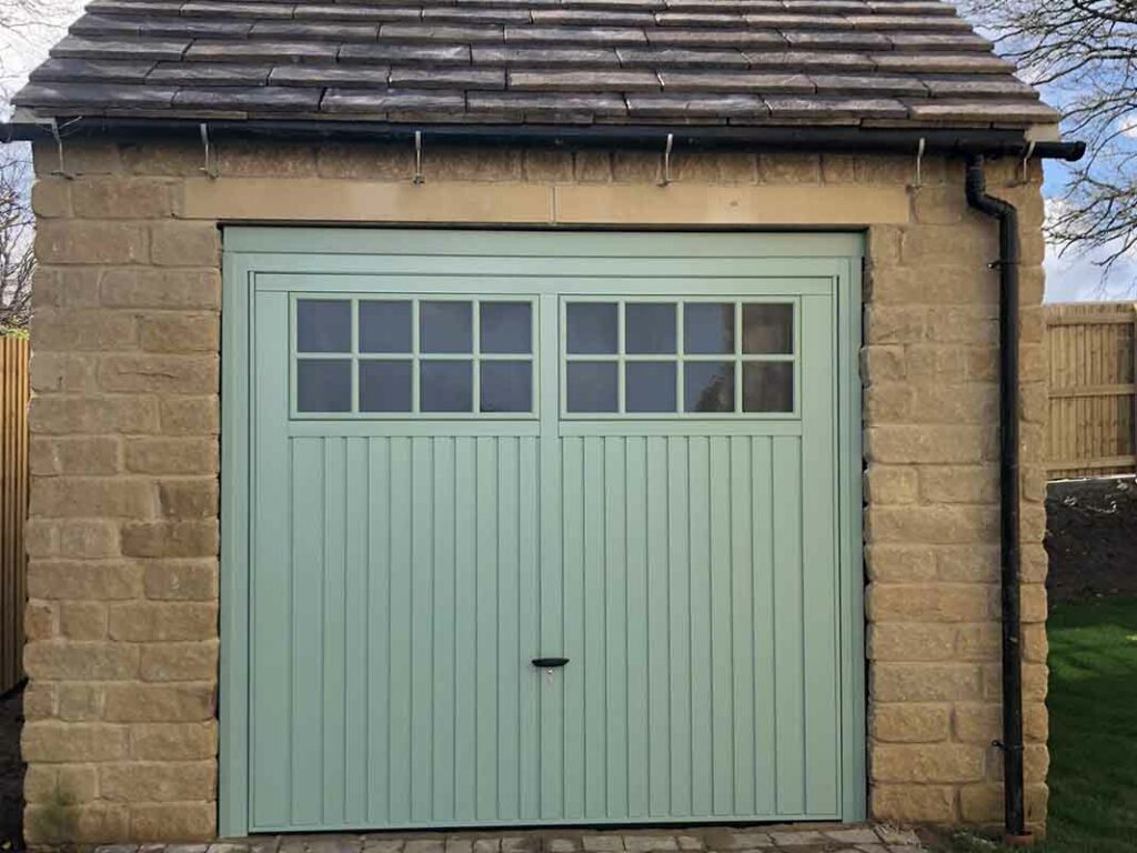 Sage green sectional garage door with windows on a stone cottage
